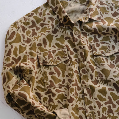 A shot of a camouflage shirt with rolled sleeves on the floor.