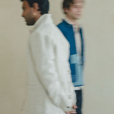 A blurry photo of two men against a neutral background walking by each other