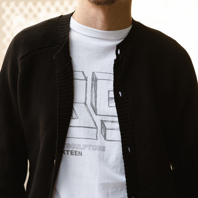 A man wears the Playscapes tee under a black cardigan.