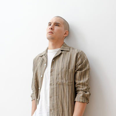 A man in a striped olive shirt leans against a wall