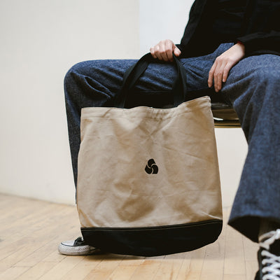 A man holds a tan tote bag.