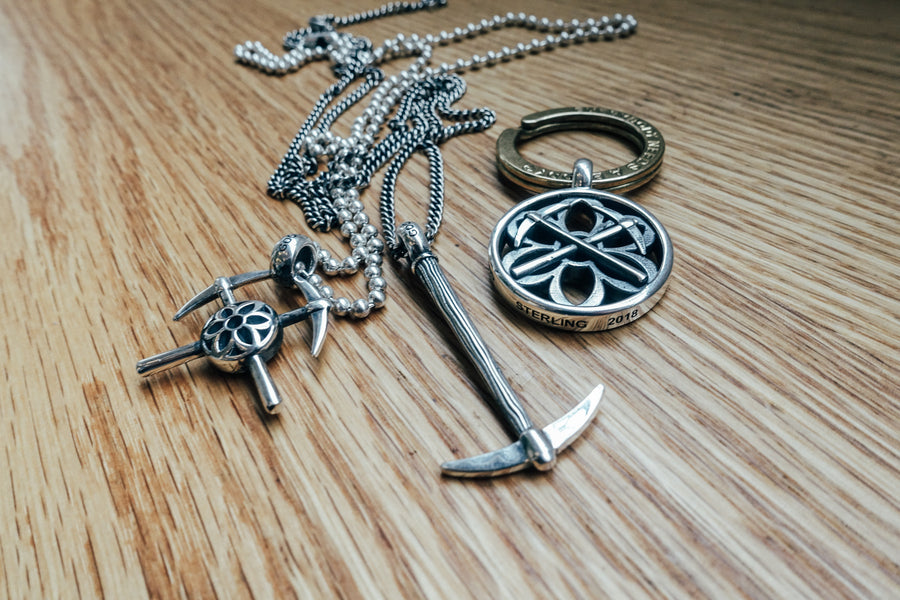 Three sterling silver pendants on chain necklaces piled up on a wood bench.