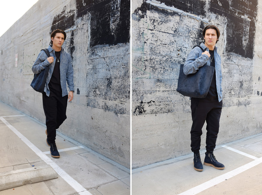 The model poses with the Viberg boots with a light blue chambray and black sweatpants, while holding the Viberg tote that is made of the same leather.
