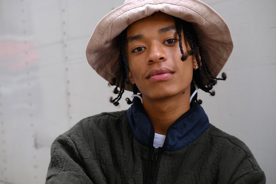 A portrait of a young man in a khaki bucket hat.