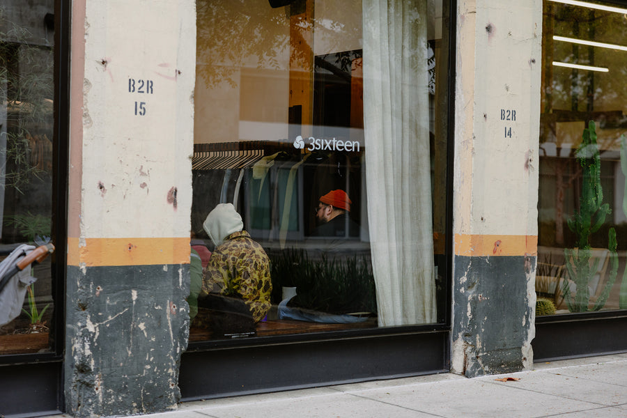 A photo of a concrete and glass storefront with a 3sixteen decal on the window.