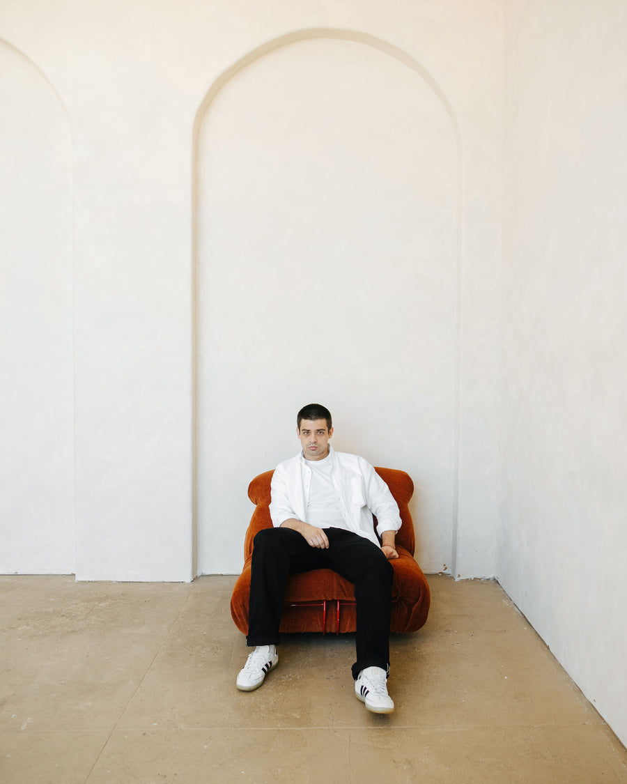 A man in a white shirt and black jeans sits on a red couch