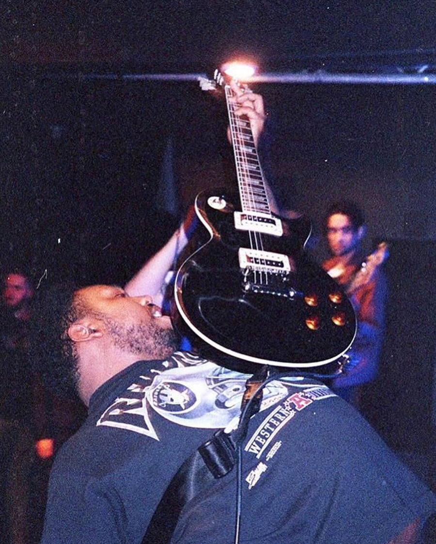 A guitar player brandishes his instrument above his body in a dramatic fashion.