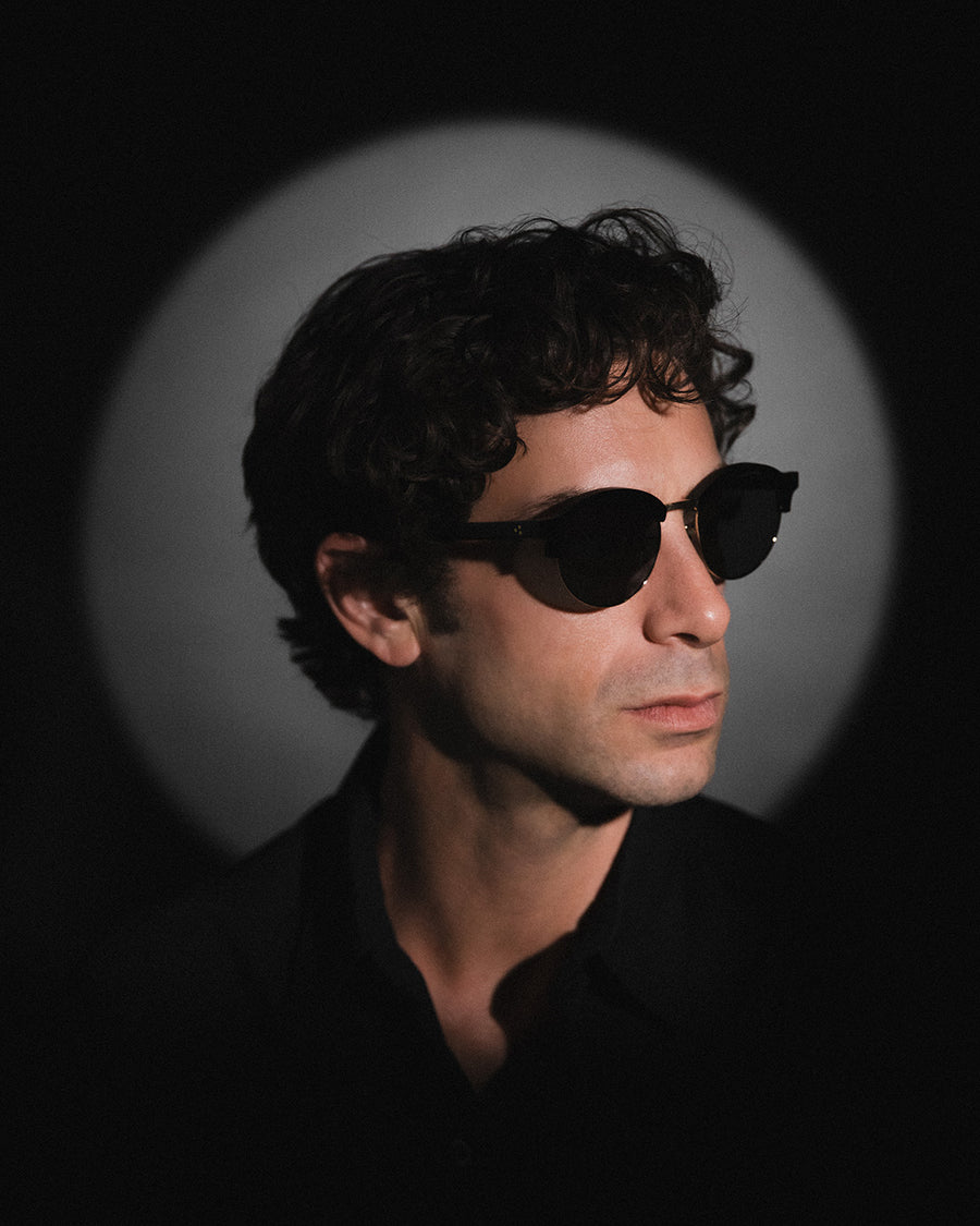 A man in acetate and wire frame glasses against a round spotlight.