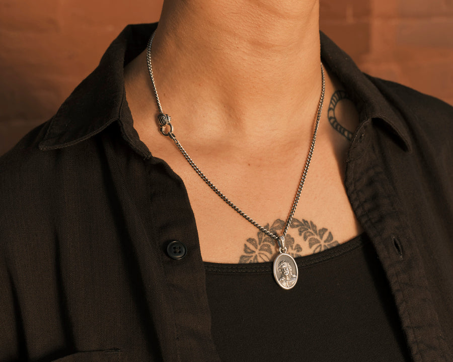 A silver curb chain with a Jesus head pendant around a woman's neck.