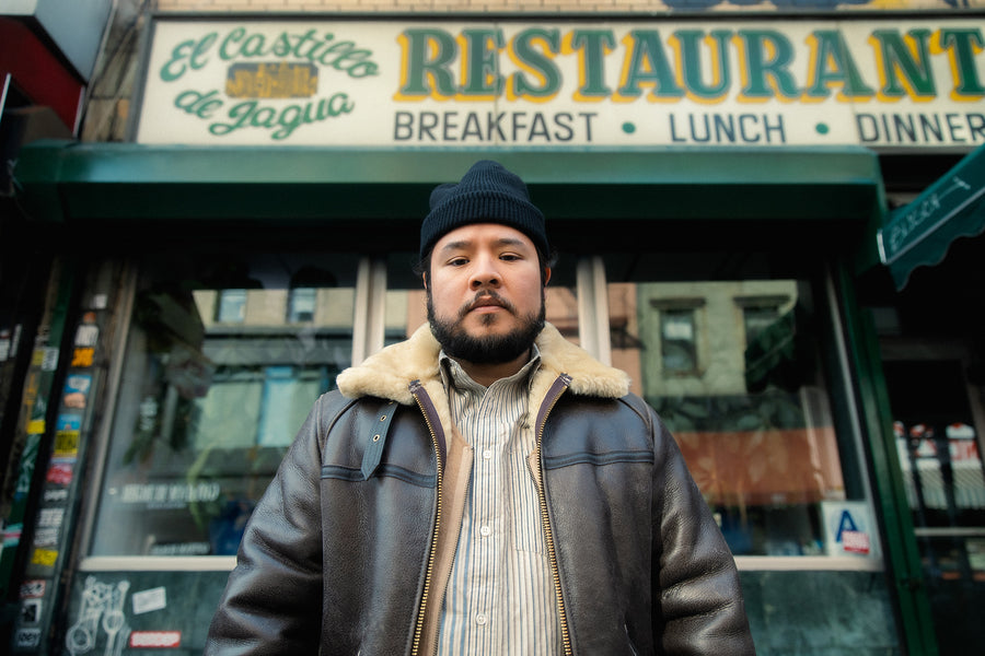 A man in a leather shearling bomber stands outside a restaurant.