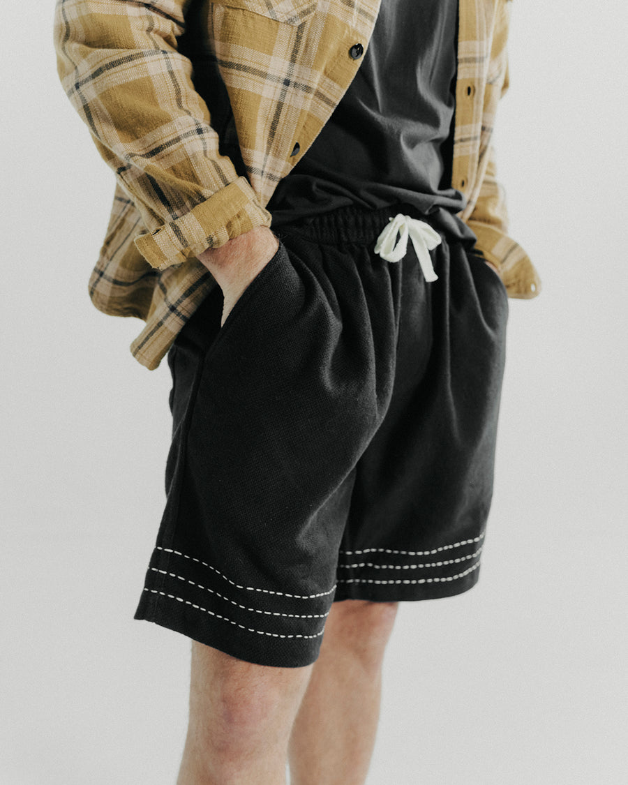 A close up detail shot of a yellow plaid flannel and black shorts.