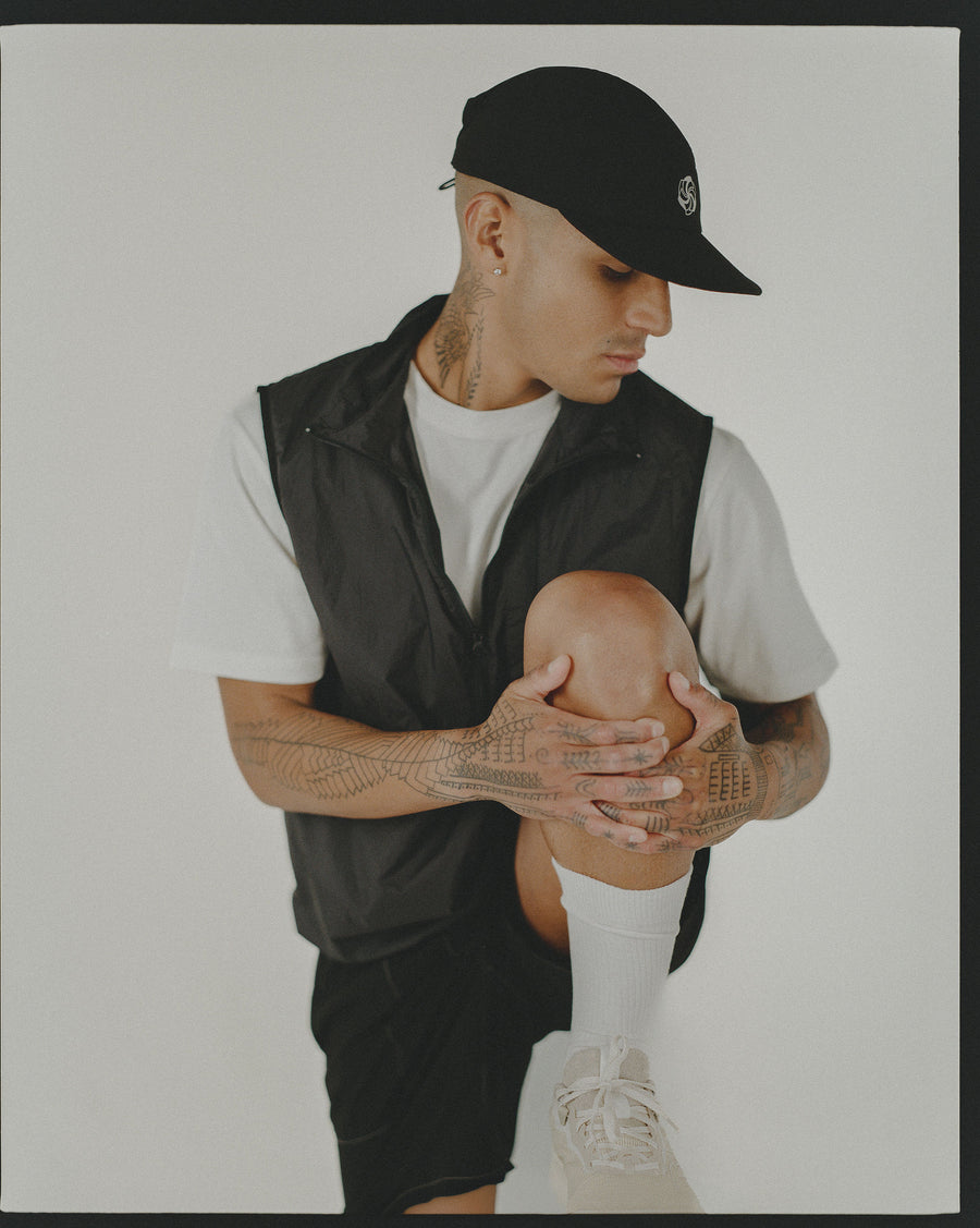 A man performs a knee hug stretch in a black nylon vest