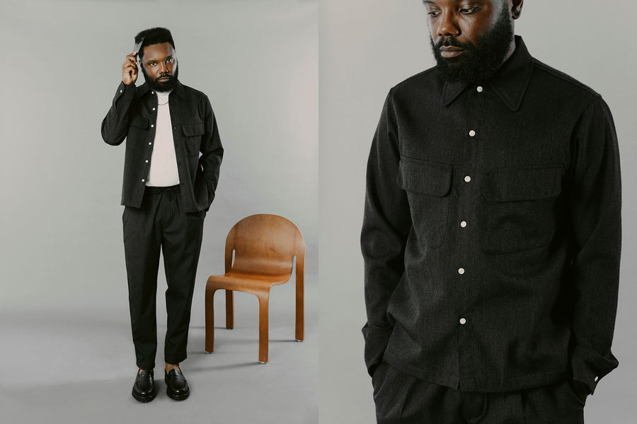 A man in a charcoal shirt and pants picks his hair out.