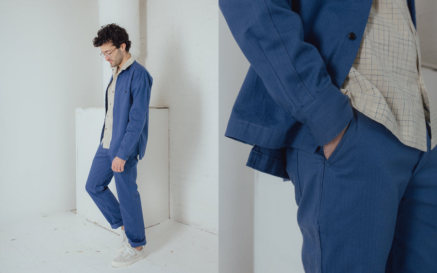 A man in a french blue herringbone twill suit walks off camera.