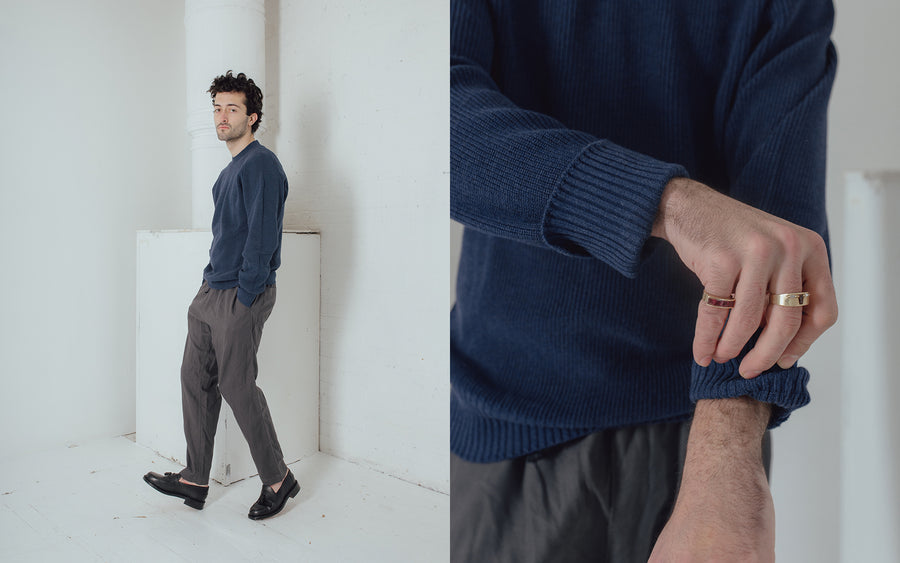 A man in a navy sweater and grey pants walks left.