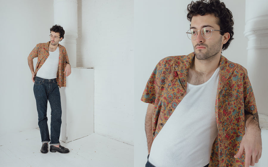 A man in an open leisure shirt leans against a column.