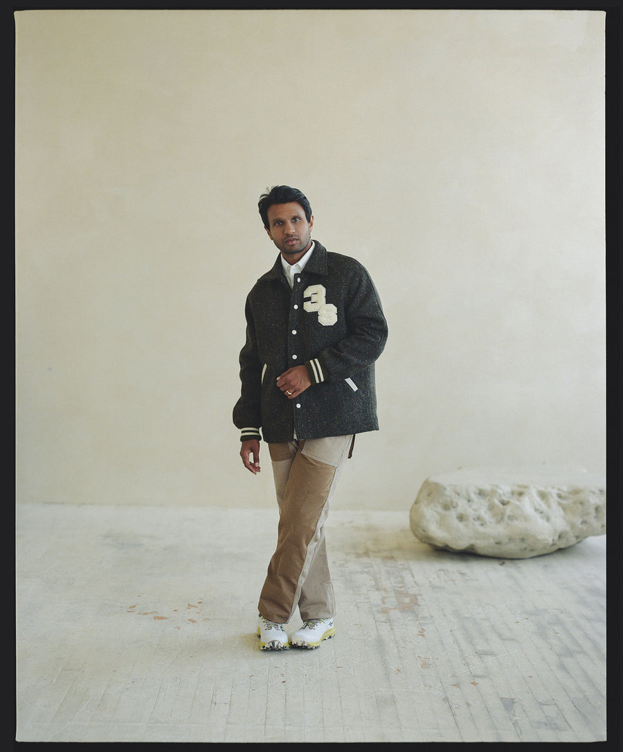 A man in a wool tweed collared jacket stands in a neutral room.