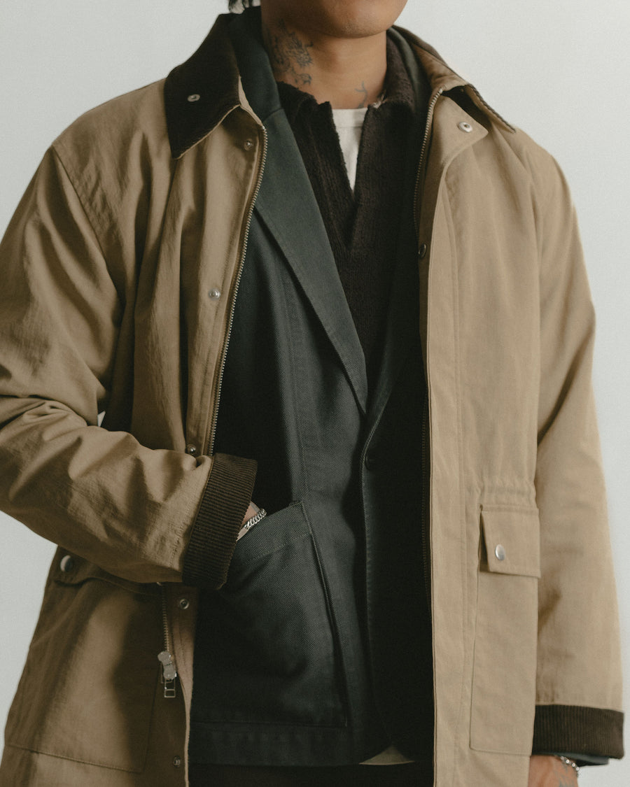 A close up shot of a tan jacket layered over a grey blazer and brown polo sweater.