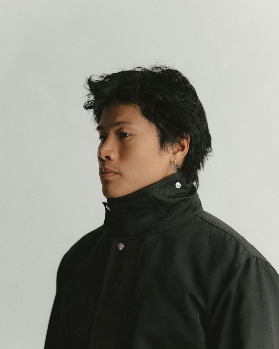 A portrait of a man in a black jacket with the collar buttoned all the way up across the neck.