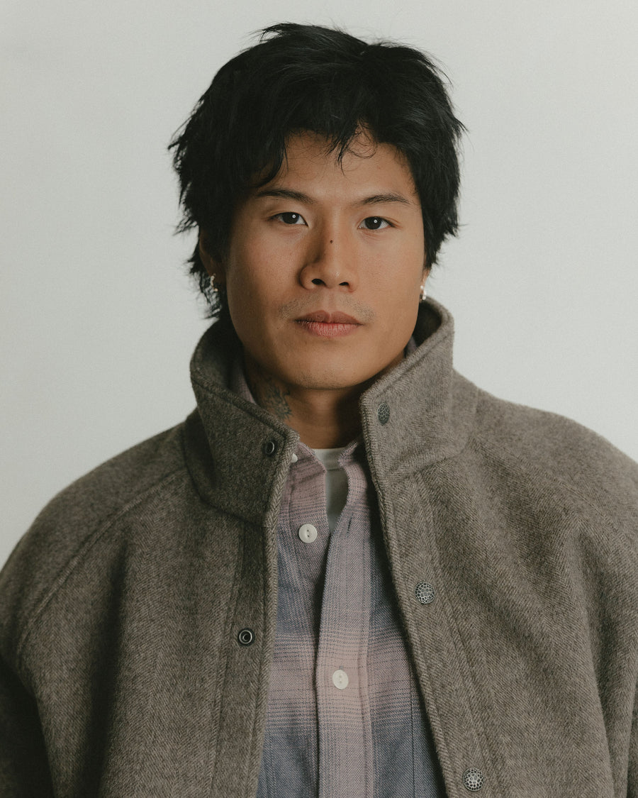 A portrait of a man wearing a pink flannel shirt with a wool coat layered on top.