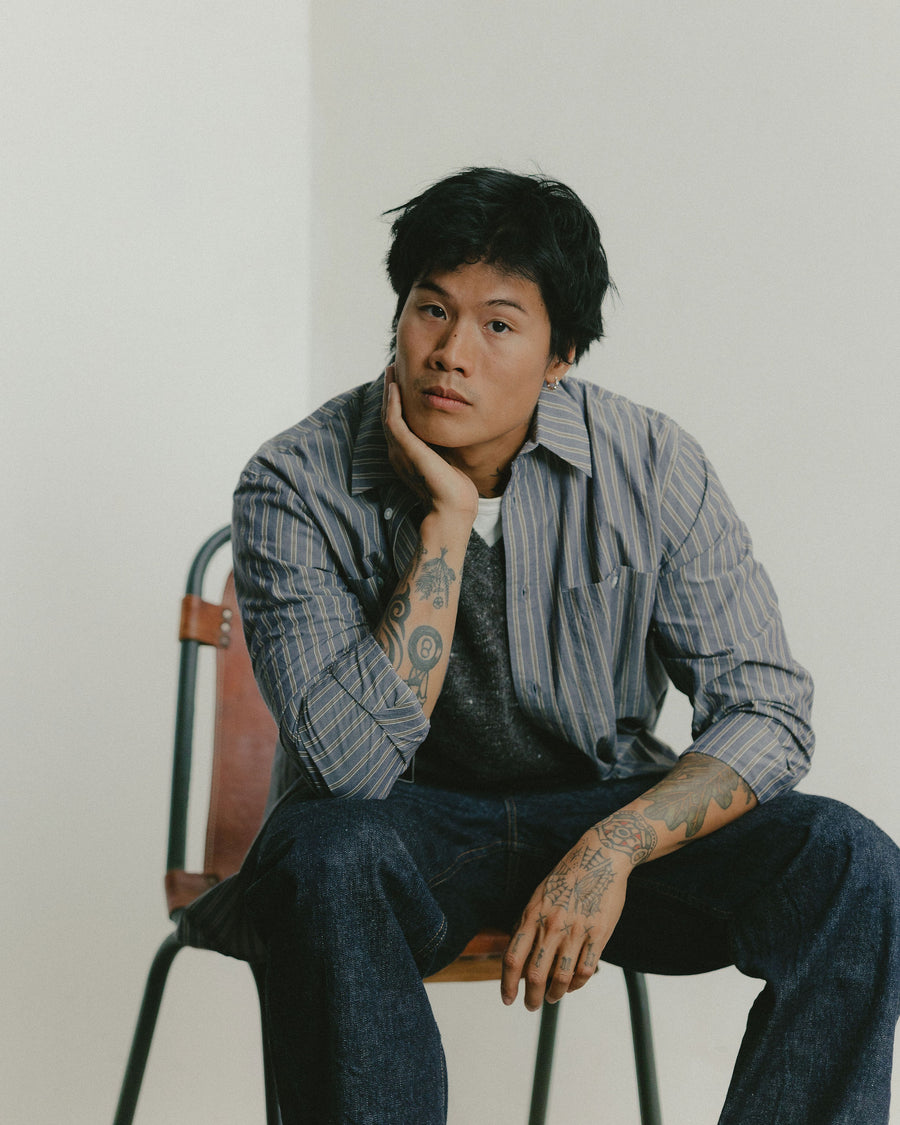 A man sits in a leather chair with a striped blue shirt.