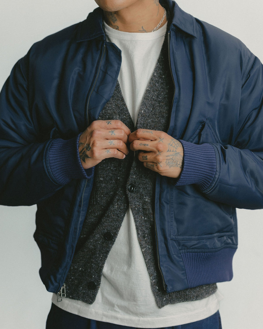 A close up shot of a blue satin bomber jacket layered over a grey cardigan.