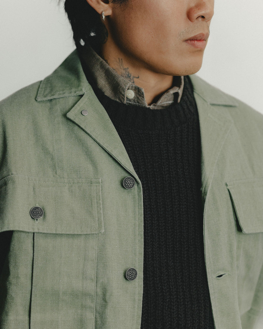 A close up shot of an olive military overshirt layered over a brown sweater.