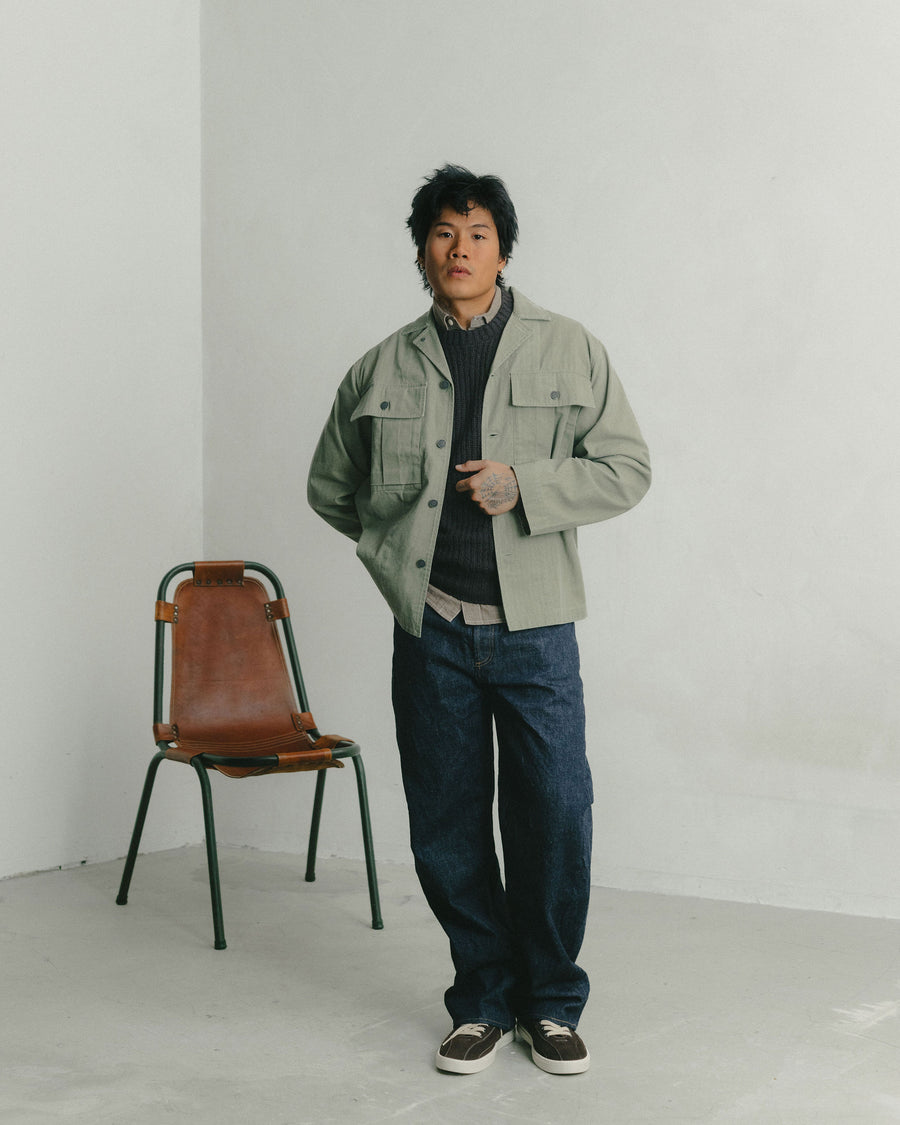 A man in a olive military overshirt and dark blue jeans poses for the camera.