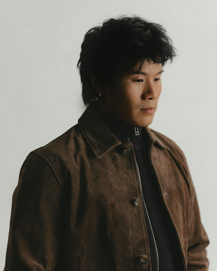 A close up shot of a brown suede jacket layered over a black full zip sweater.