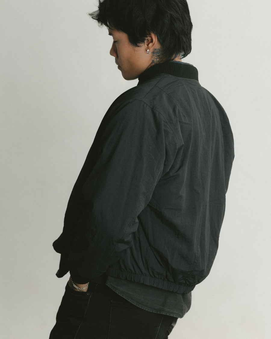 A shot of the back of a black nylon bomber jacket.