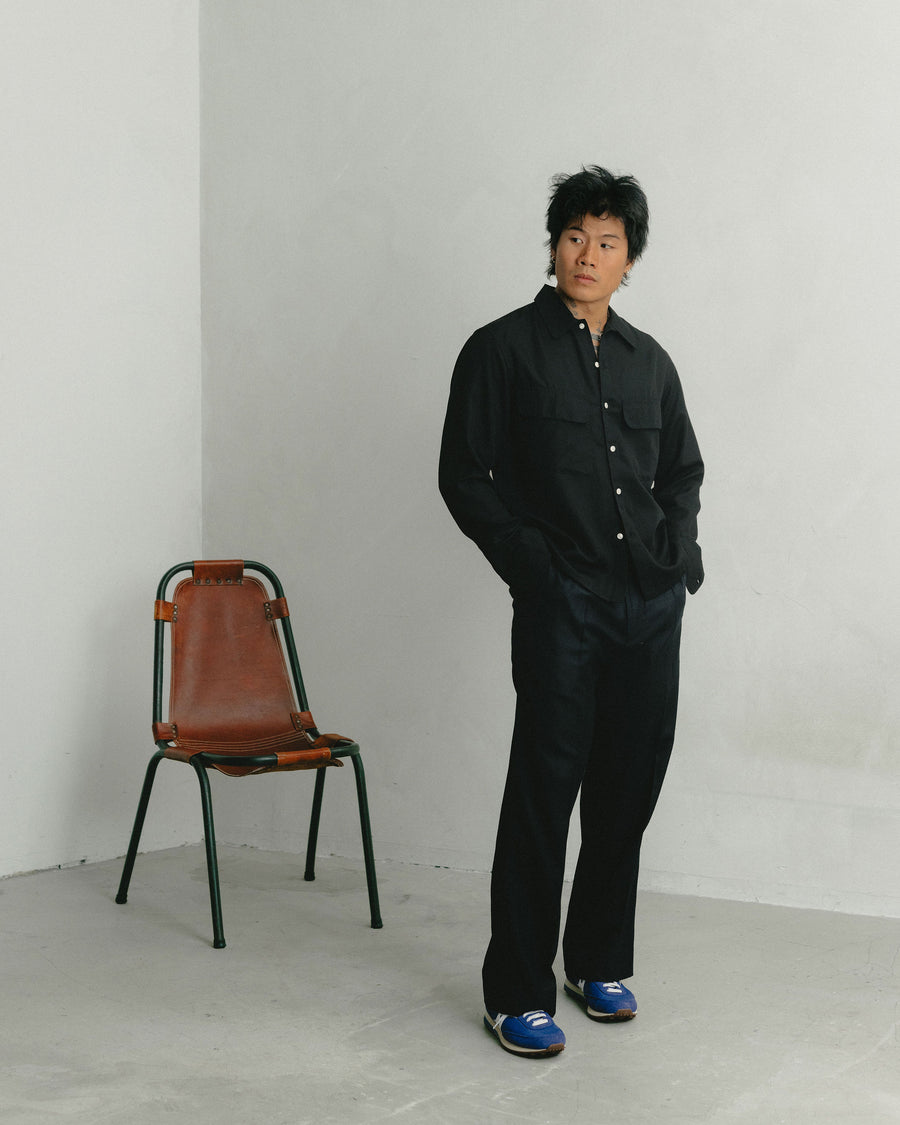 A man in a black button down and black wool trousers.