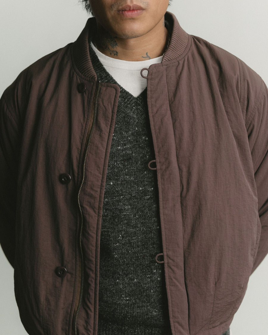 A close up shot of a brown nylon bomber jacket layered over a grey sweater.