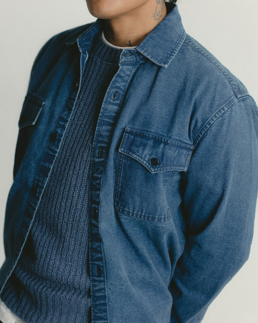 A close up detail shot of a washed out blue canvas shirt layered over a slate knit sweater.
