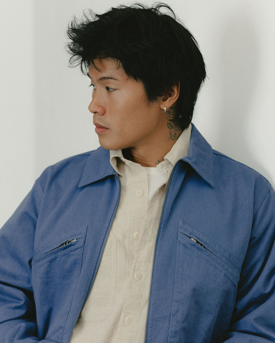 A close up portrait of a man wearing a light blue jacket worn over an ecru chambray shirt.