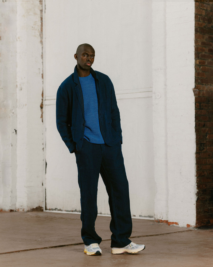 A man in a navy suit with a light blue sweater layered underneath.