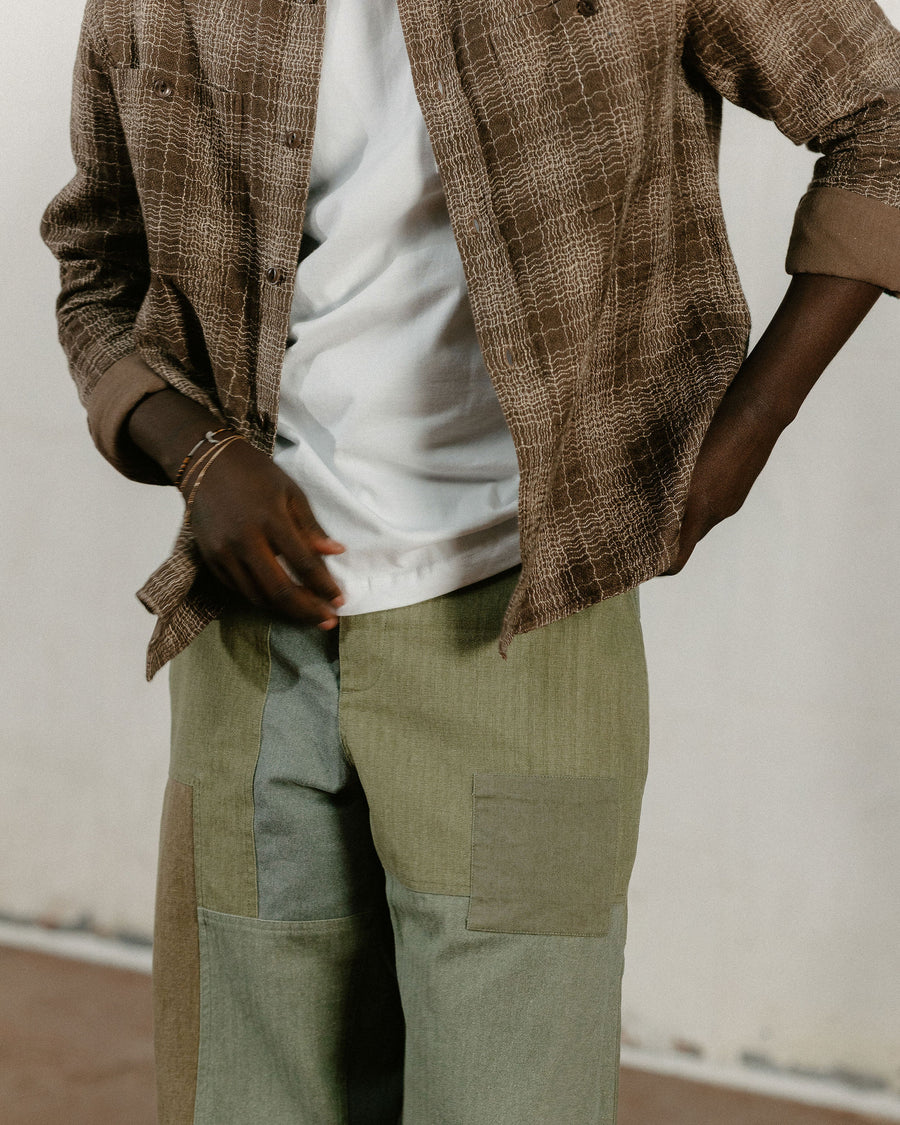 A close up of the waist of a man wearing a brown check shirt and olive patchwork pants.