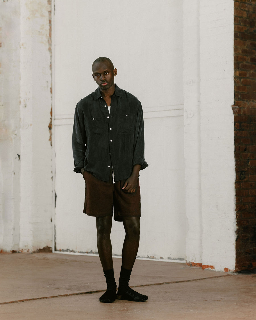 A man in a flowy black shirt and brown shorts.