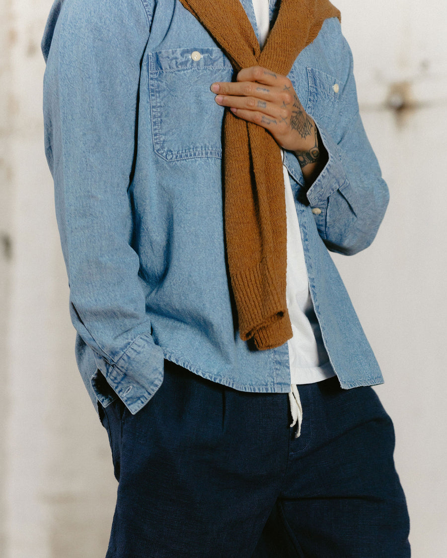 A detail shot of a tan sweater draped over a blue chambray shirt.