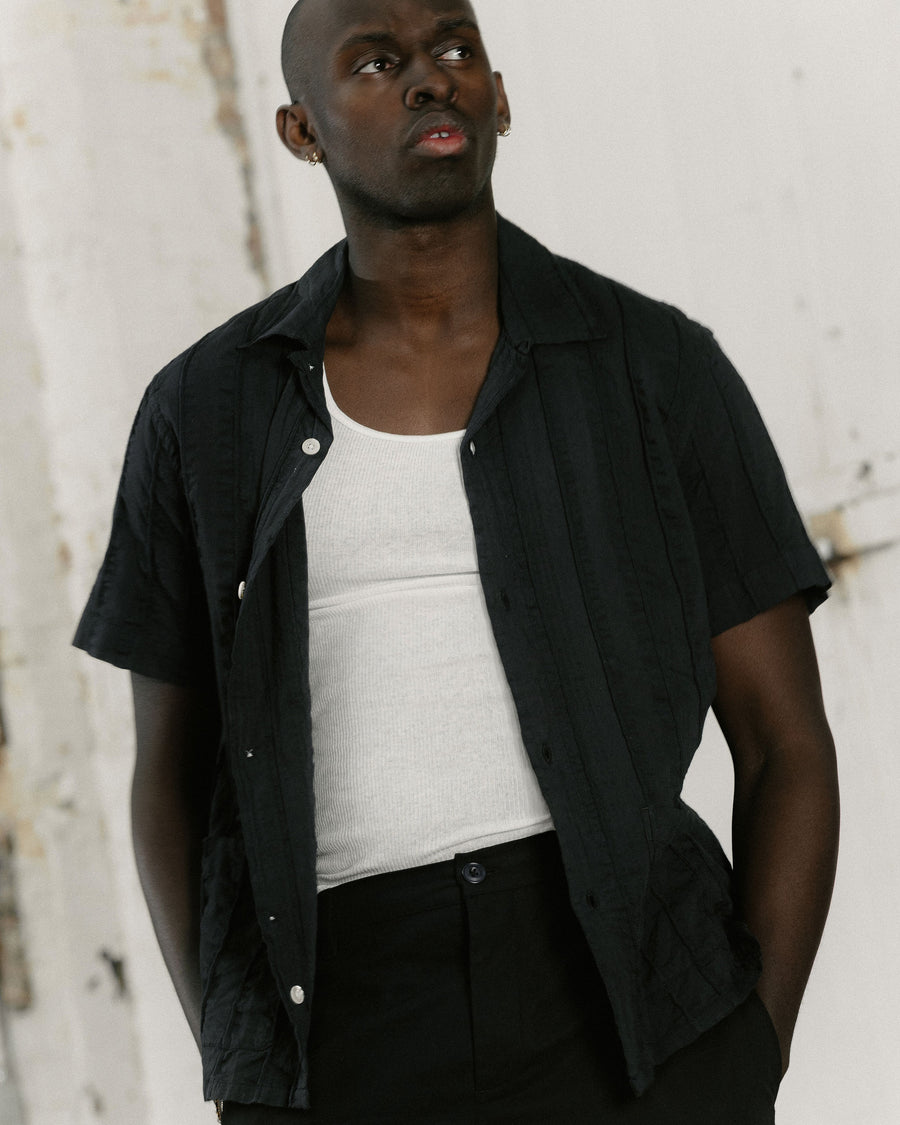 A close up image of a man in a black short sleeve button down.