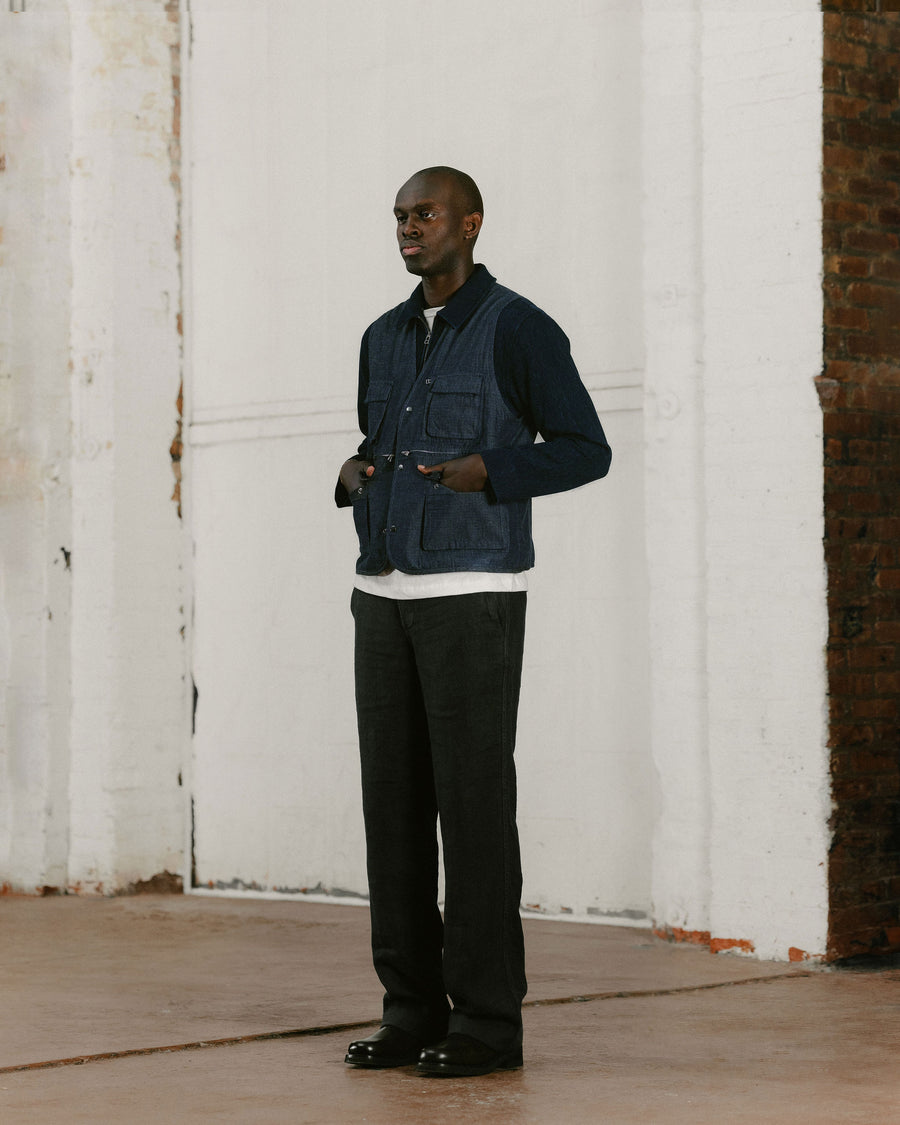 A man in a navy vest and navy pants looks to the left.