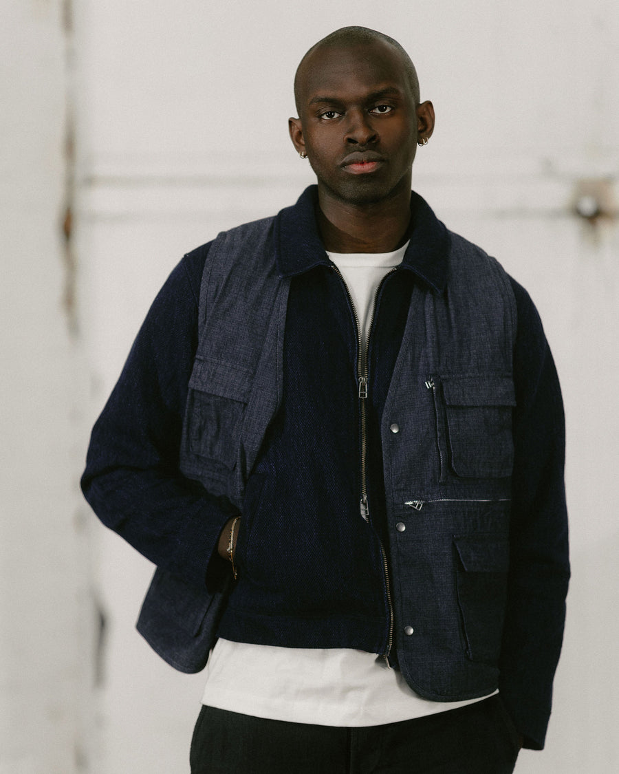 A man with a navy vest layered over a navy jacket looks into the camera.