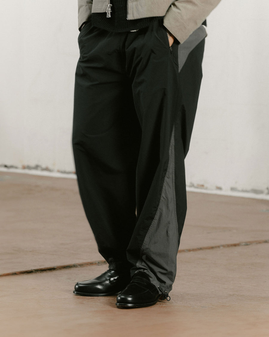 A detail photo of black and grey paneled nylon track pants worn with loafers.
