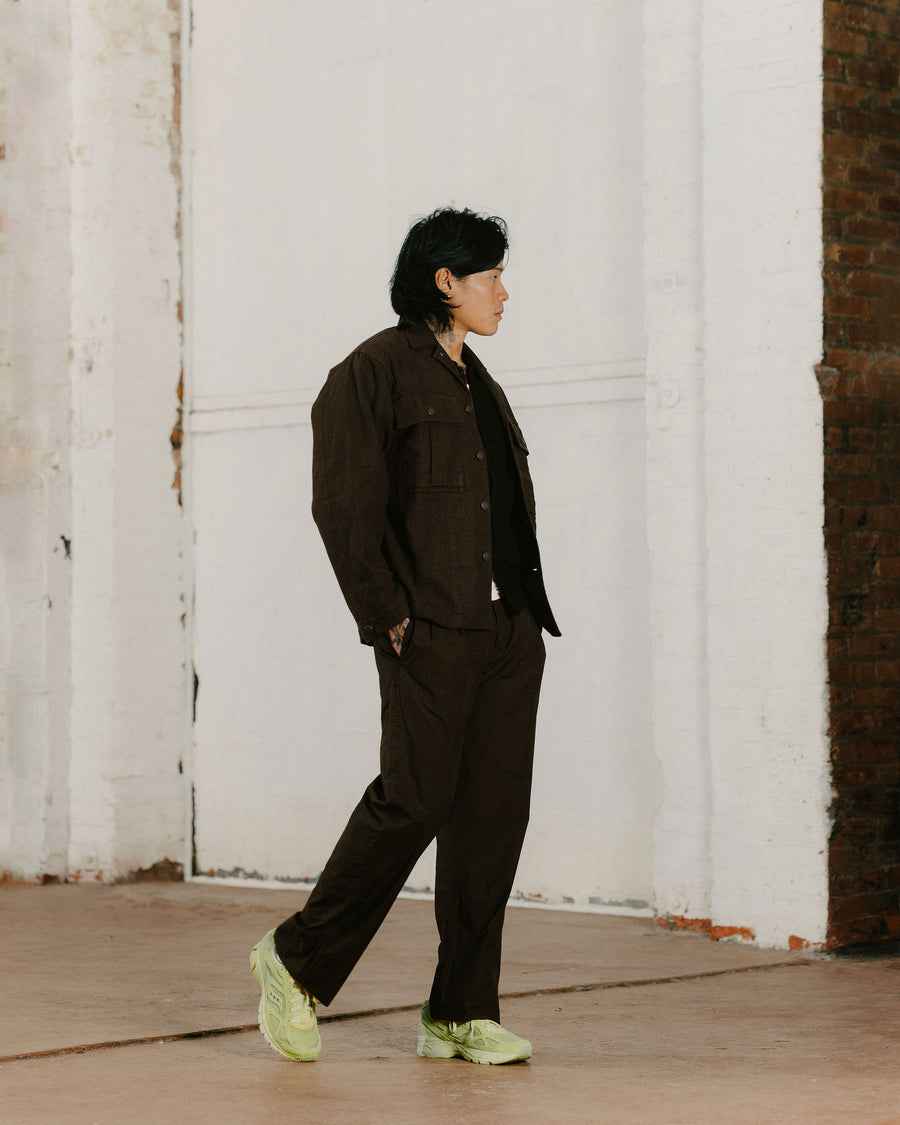 A man in a dark brown top and pants and neon green sneakers.