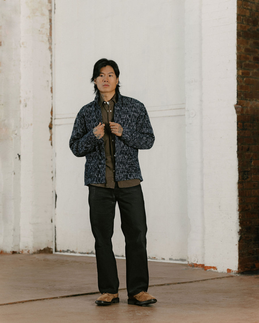 A man in a heathered black chore coat and black pants.