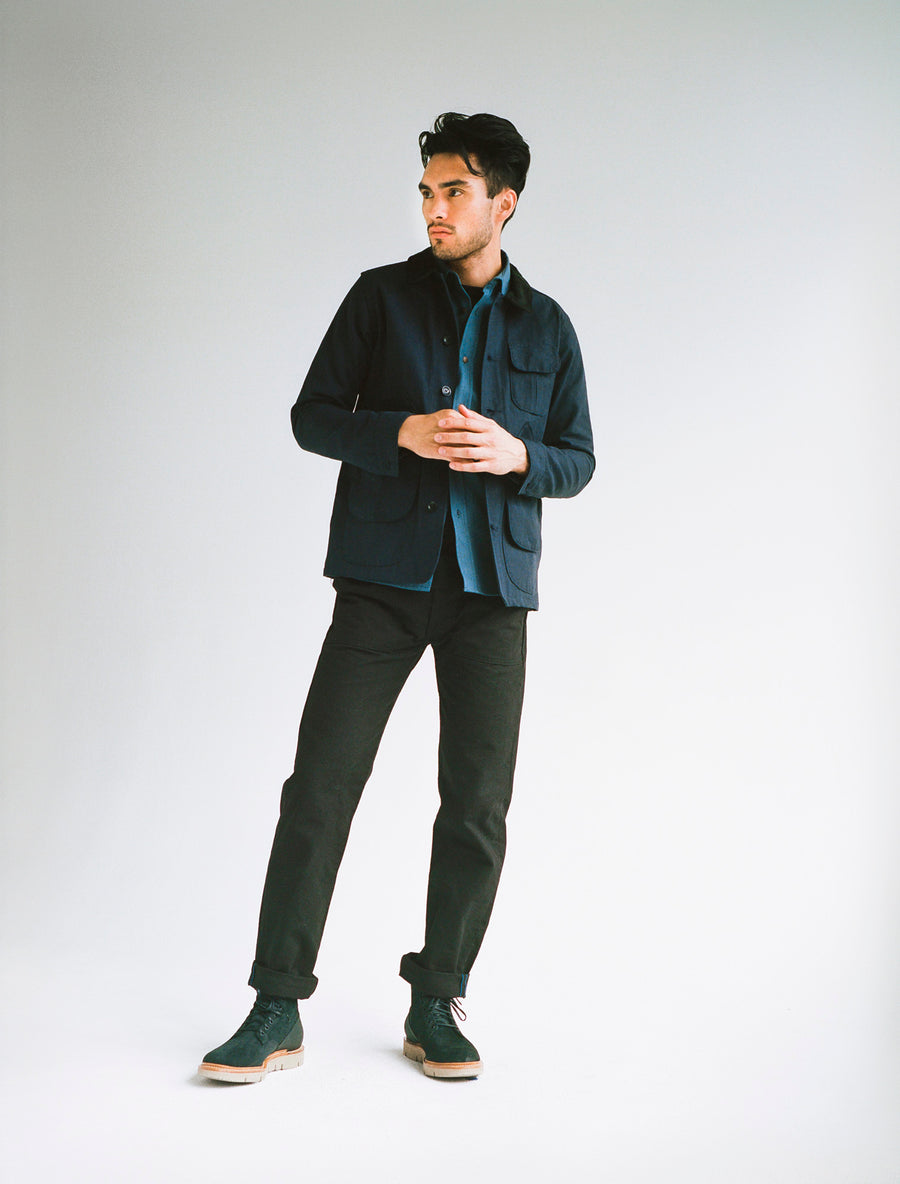 Model wears a navy hunting jacket, slate blue shirt, and black pants.