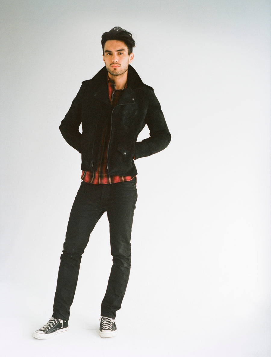 Model wears a red plaid flannel underneath a black leather jacket, coupled with black slim jeans.