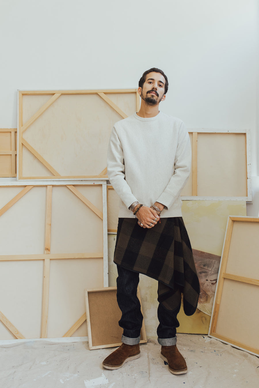 A man stands in front of a number of art canvases modeling clothing.