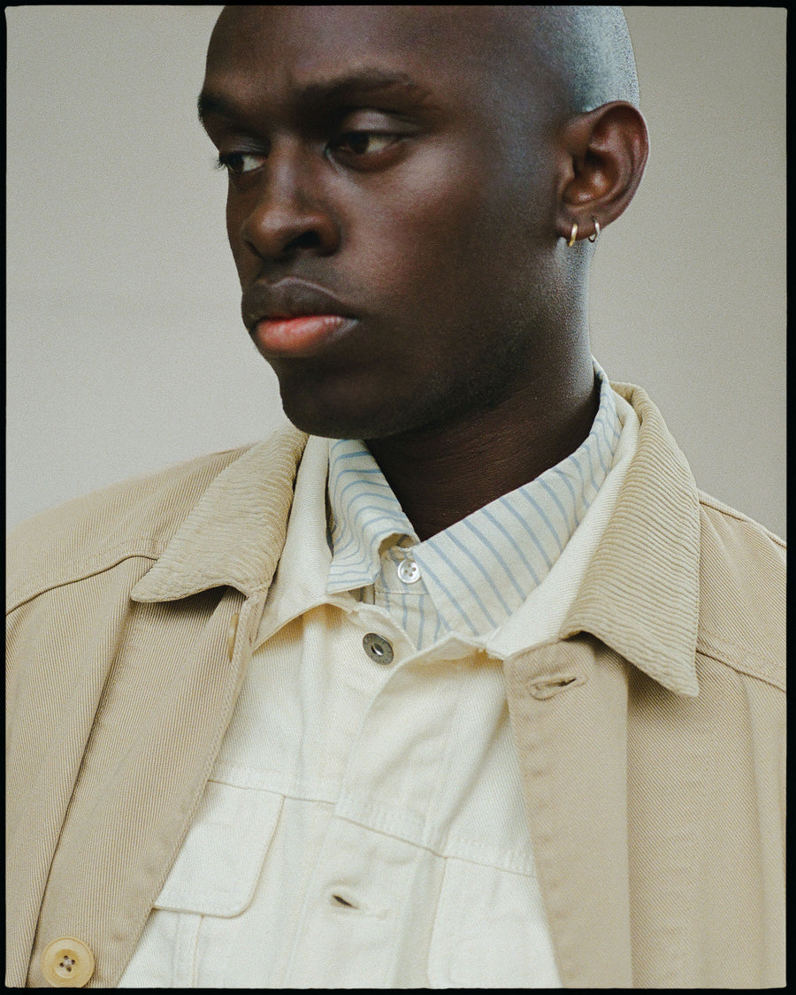 A man in a cream colored shirt, denim jacket and tan outerwear jacket.