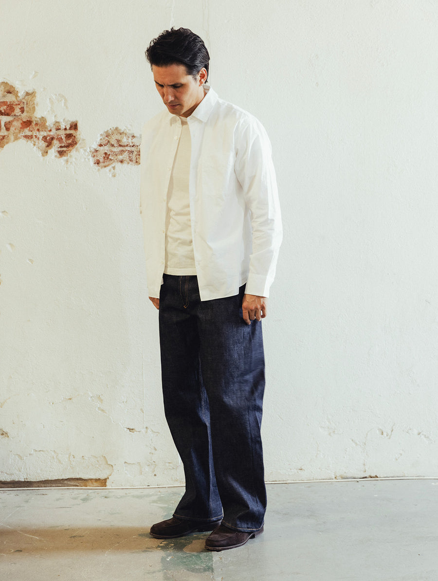 A man in a white dress shirt and blue jeans models some jeans.