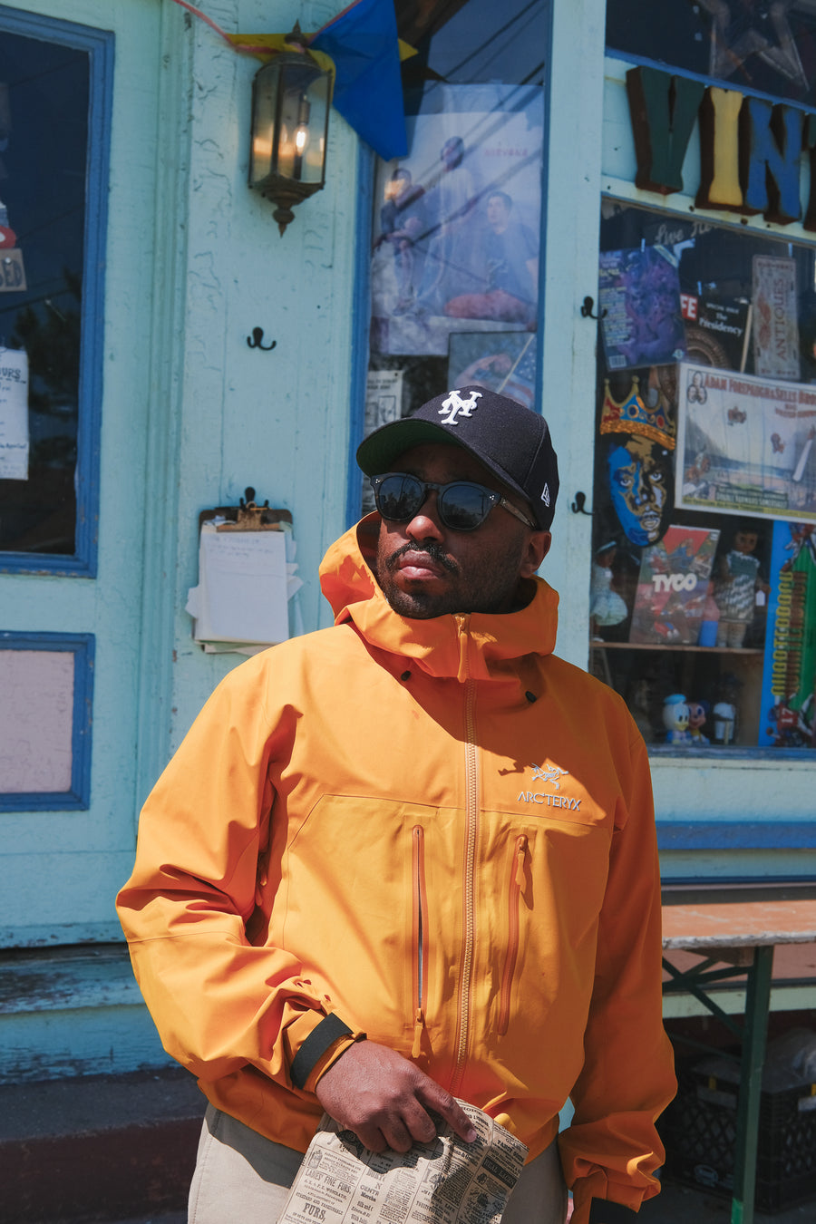 A man in a yellow jacket outside a cyan storefront.